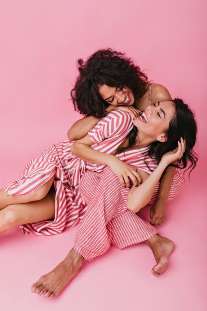 Mooie donkere meisjes, schattige looks met een vrolijke glimlach. Jonge dames in roze gestreepte pyjama poseren.