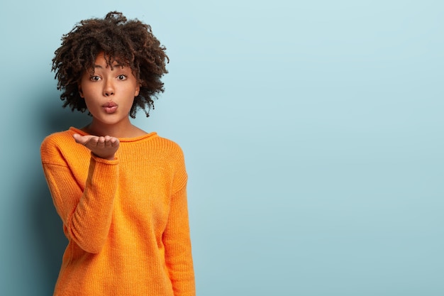 Mooie donkere vrouw met Afro-haar stuurt luchtkus naar geliefde vriend, vouwt de lippen, handpalm uitgestrekt