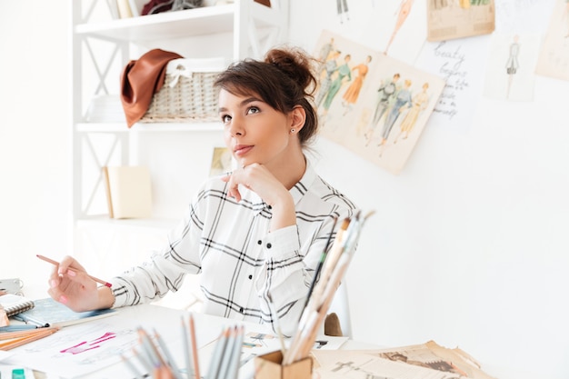 Mooie doordachte vrouw modeontwerper zittend op haar werkplek