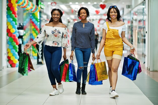 Mooie drie goed geklede Afro-Amerikaanse meisjes met gekleurde boodschappentassen wandelen in winkelcentrum