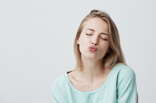 Mooie dromerige vrouw met blond haar sluit ogen, pruilt lippen, stuurt kusjes