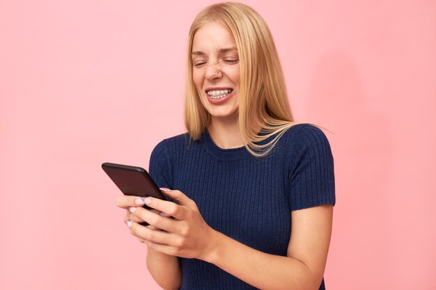 Mooie emotionele jonge Europese vrouw met haakjes tanden en sproeten online chatten met vrienden via applicatie op mobiel