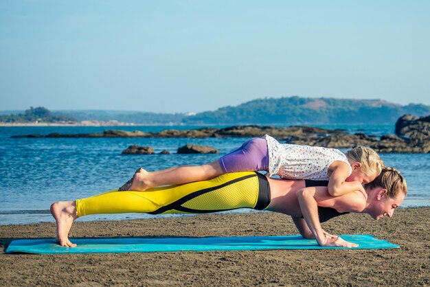 Mooie en flexibele moeder en charmante dochter die yoga beoefent en rekoefeningen doet op het strand.