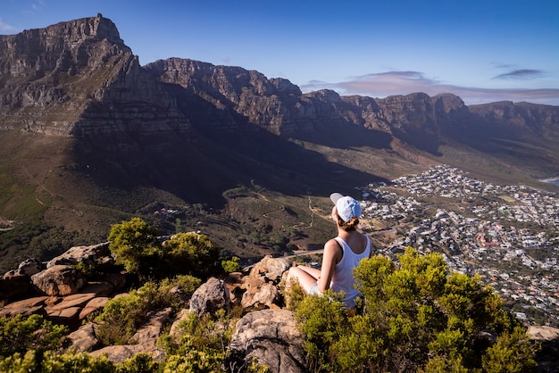 Mooie foto van een onherkenbare vrouw die op de rand van een klif zit en de stad Kaapstad bewondert