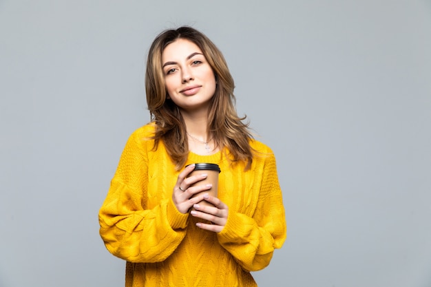 Mooie gelukkige jonge vrouw die over grijze muur het drinken koffie wordt geïsoleerd.