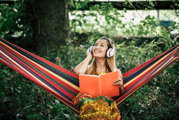Mooie gelukkige jonge vrouw met hoofdtelefoons die aan muziek luisteren en een boek lezen