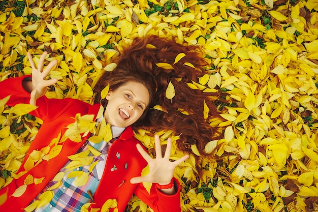 Mooie gelukkige vrouw die in gele de herfstbladeren legt.