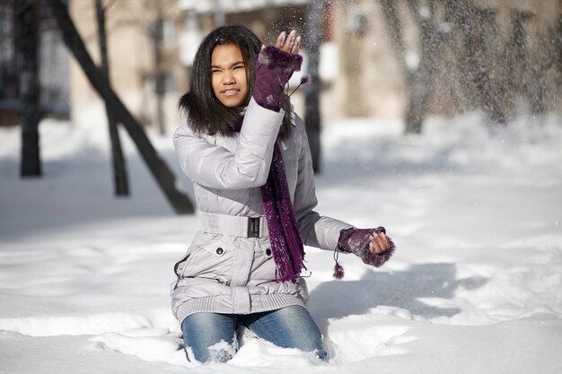 Mooie glimlachende amerikaanse meisjeszitting in sneeuw die in openlucht met sneeuw speelt