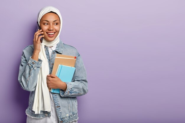 Mooie glimlachende Arabische vrouw voert een telefoongesprek, kijkt opzij, bespreekt het laatste nieuws met groepsgenoot via mobiel