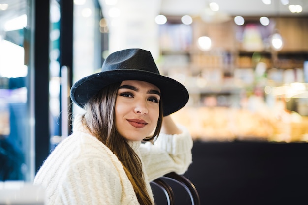 Gratis foto mooie glimlachende jonge vrouw die zwarte hoed op hoofd draagt