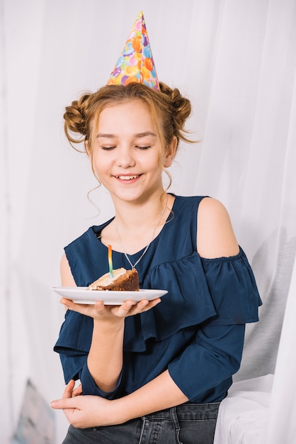 Mooie glimlachende tiener die plak van cake op plaat bekijkt