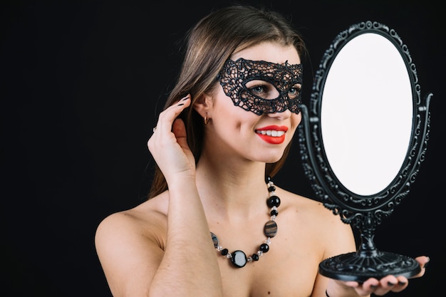 Gratis foto mooie glimlachende vrouw die in carnaval masker in hand spiegel kijkt