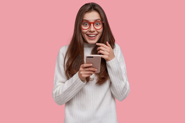 Mooie glimlachende vrouw stuurt bericht op moderne mobiel, in hoge geest, terloops gekleed, verbonden met draadloos internet