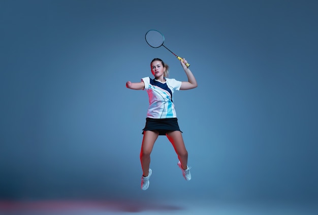 Mooie handicap vrouw oefenen in badminton geïsoleerd op blauwe achtergrond in neonlicht. Levensstijl van inclusieve mensen, diversiteit en gelijkheid. Sport, activiteit en beweging. Copyspace voor advertentie.