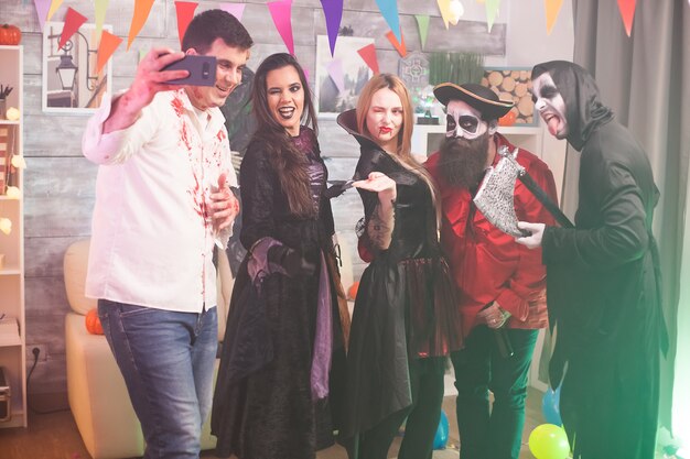 Mooie heks knipoogt terwijl de zombie een selfie neemt op halloween-feest. Spookachtige kostuums.