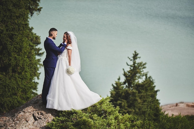 Mooie huwelijksfoto op bergmeer. gelukkig aziatisch verliefd stel, bruid in witte jurk en bruidegom in pak worden gefotografeerd tegen de achtergrond van het kazachse landschap