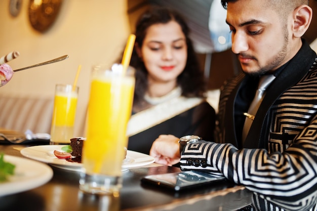 Mooie Indiase verliefde paar dragen bij saree en elegant pak zittend op restaurant Op tafel zoete desserts en sappen Man kijken naar zijn horloges