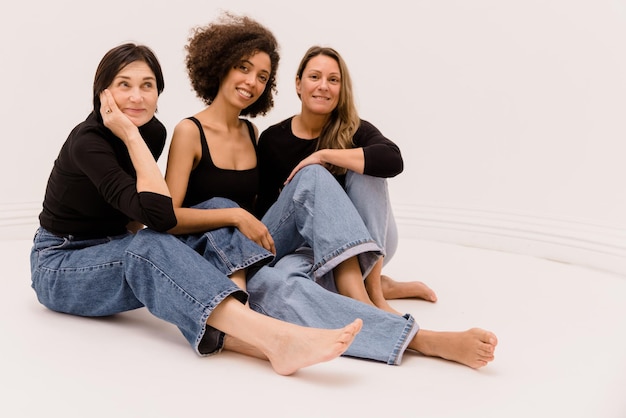 Mooie interraciale en gemengde leeftijdsvrouwen in vrijetijdskleding zittend op de vloer van een witte achtergrond Lifestyle concept