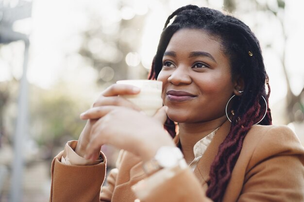 Mooie jonge Afro-Amerikaanse vrouw die op het terras zit en koffie drinkt
