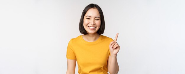 Mooie jonge aziatische vrouw die met de vinger omhoog lacht en geamuseerd kijkt naar de camera met reclame...