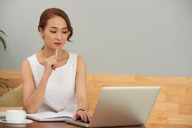 Mooie jonge Aziatische vrouwenzitting thuis en werkend aan laptop