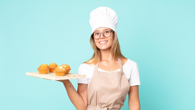 Mooie jonge blonde chef-kok vrouw met een dienblad met muffins