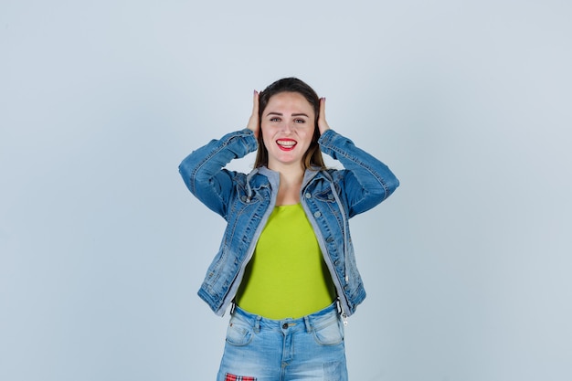 Mooie jonge dame die de oren in een denim-outfit houdt en er blij uitziet, vooraanzicht.