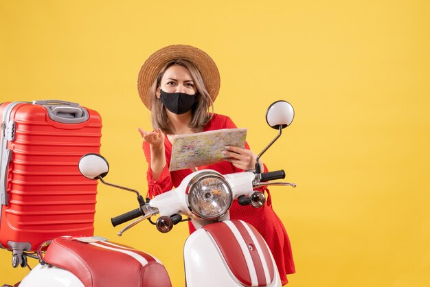 mooie jonge dame met zwart masker met kaart in de buurt van bromfiets