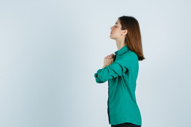 Mooie jonge dame omklemde handen in biddend gebaar in groen overhemd en op zoek hoopvol.