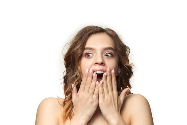 Mooie jonge lachende vrouw met lang golvend zijdeachtig haar, natuurlijke make-up met hand in de buurt van kin geïsoleerd op een witte muur. Model met frisse glanzende huid en natuurlijke make-up. Emoties van mensen