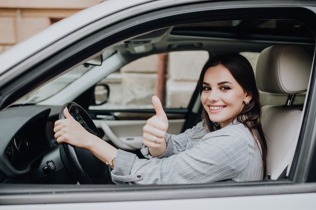 Gratis foto mooie jonge latijnse vrouw die haar gloednieuwe auto drijft en haar duim toont