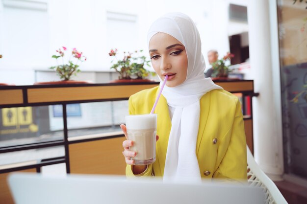 Mooie jonge moslimvrouw die laptop gebruikt terwijl ze in café zit