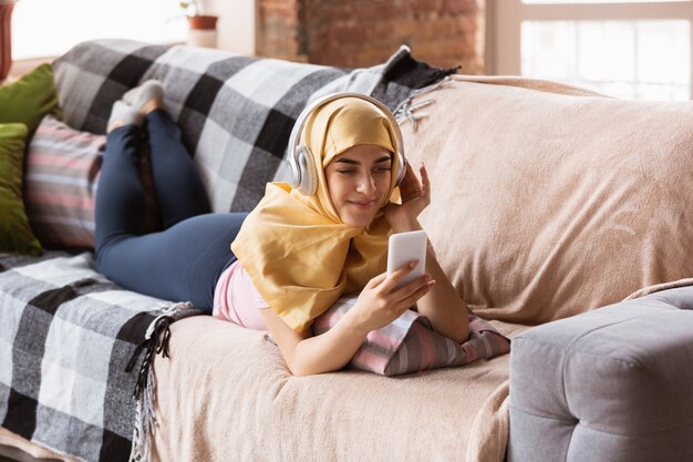 mooie jonge moslimvrouw thuis tijdens quarantaine en zelfisolatie, met tablet voor selfie of videocall, online lessen