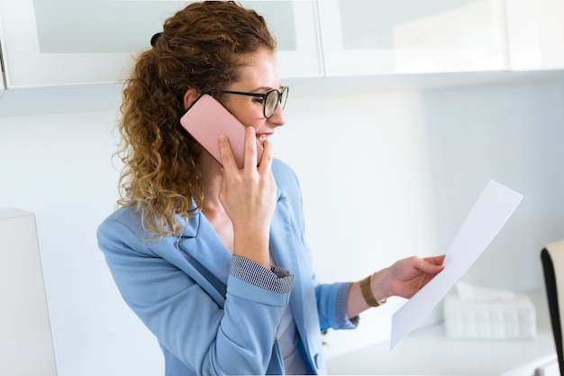 Mooie jonge onderneemster die haar mobiele telefoon in het bureau met behulp van.