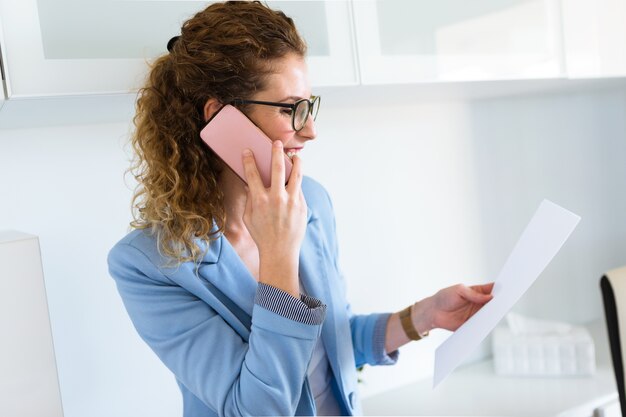 Mooie jonge onderneemster die haar mobiele telefoon in het bureau met behulp van.