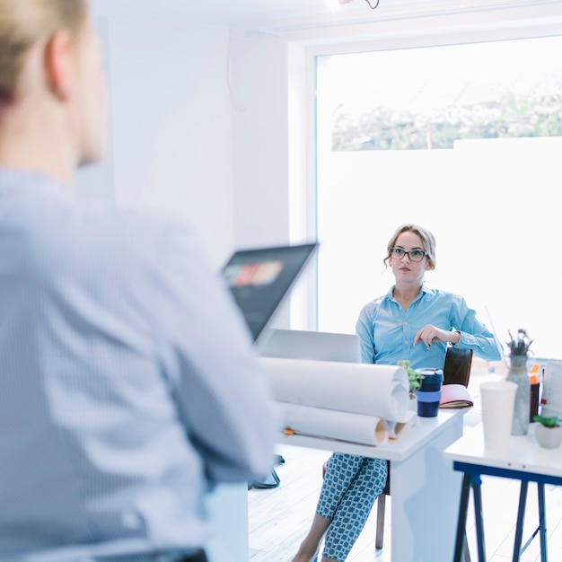 Mooie jonge onderneemsterzitting op stoel die aan haar collega in vergadering luisteren