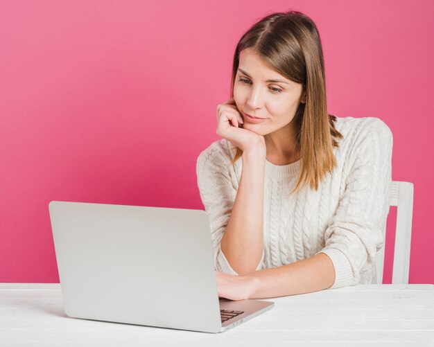 Mooie jonge vrouw die aan laptop tegen roze achtergrond werkt