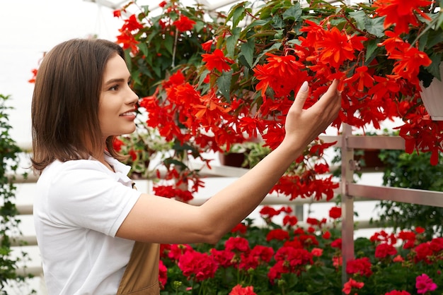 Mooie jonge vrouw die aan mooie rode bloemen snuift