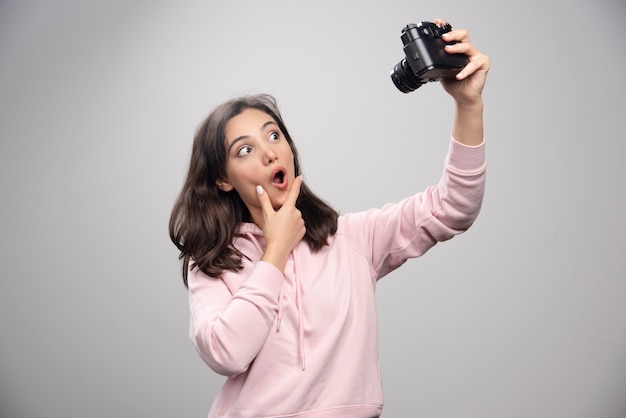 Mooie jonge vrouw die een selfie met camera neemt over een grijze muur.