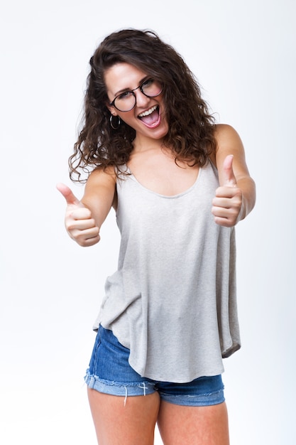 Gratis foto mooie jonge vrouw die geluk uitdrukt met duim omhoog op witte achtergrond.