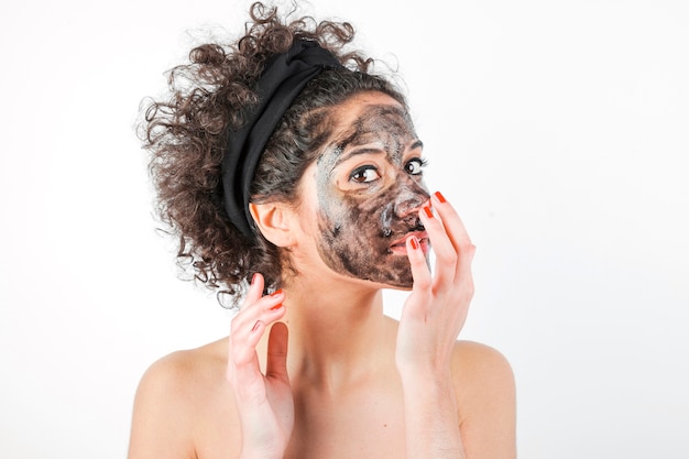 Mooie jonge vrouw die gezichtsmasker op haar gezicht over witte achtergrond toepast