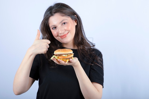 mooie jonge vrouw die heerlijke rundvleesburger houdt en duimen opgeeft.