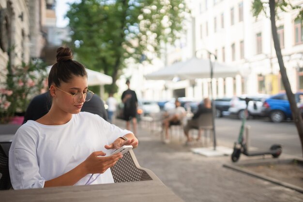 Mooie jonge vrouw die in een straatcafé zit met een smartphone