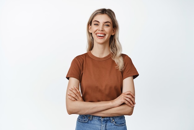Mooie jonge vrouw die lacht en glimlacht met gekruiste armen op de borst en naar de camera kijkt die in vrijetijdskleding tegen een witte achtergrond staat