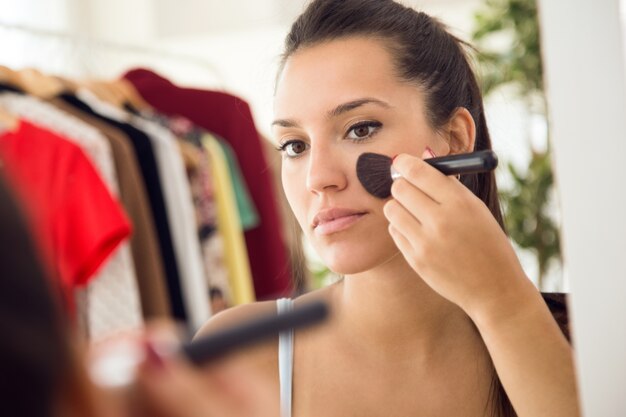 Mooie jonge vrouw die make-up dichtbij spiegel thuis maakt.