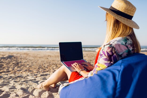 Mooie jonge vrouw die met laptop aan het tropische strand werkt