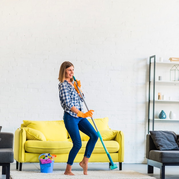 Mooie jonge vrouw die met zwabber in de woonkamer danst