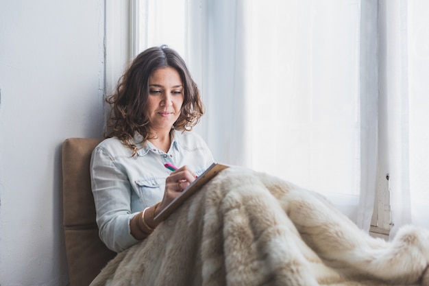 Mooie jonge vrouw die naast het raam