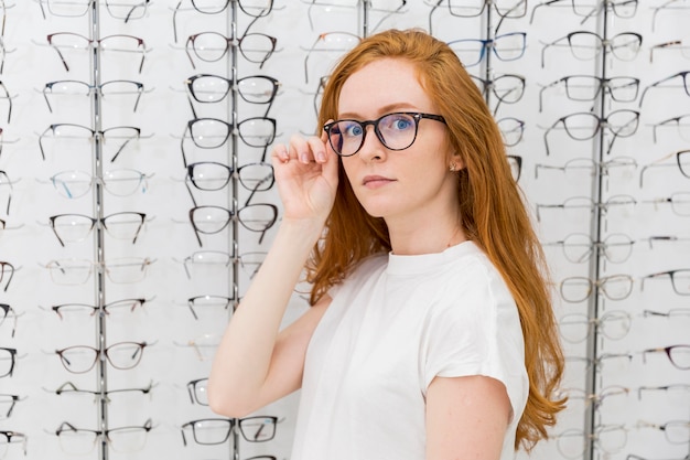 Mooie jonge vrouw die oogglazen draagt die camera in opticienwinkel bekijken