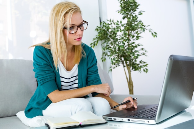 Mooie jonge vrouw die thuis met laptop werkt.